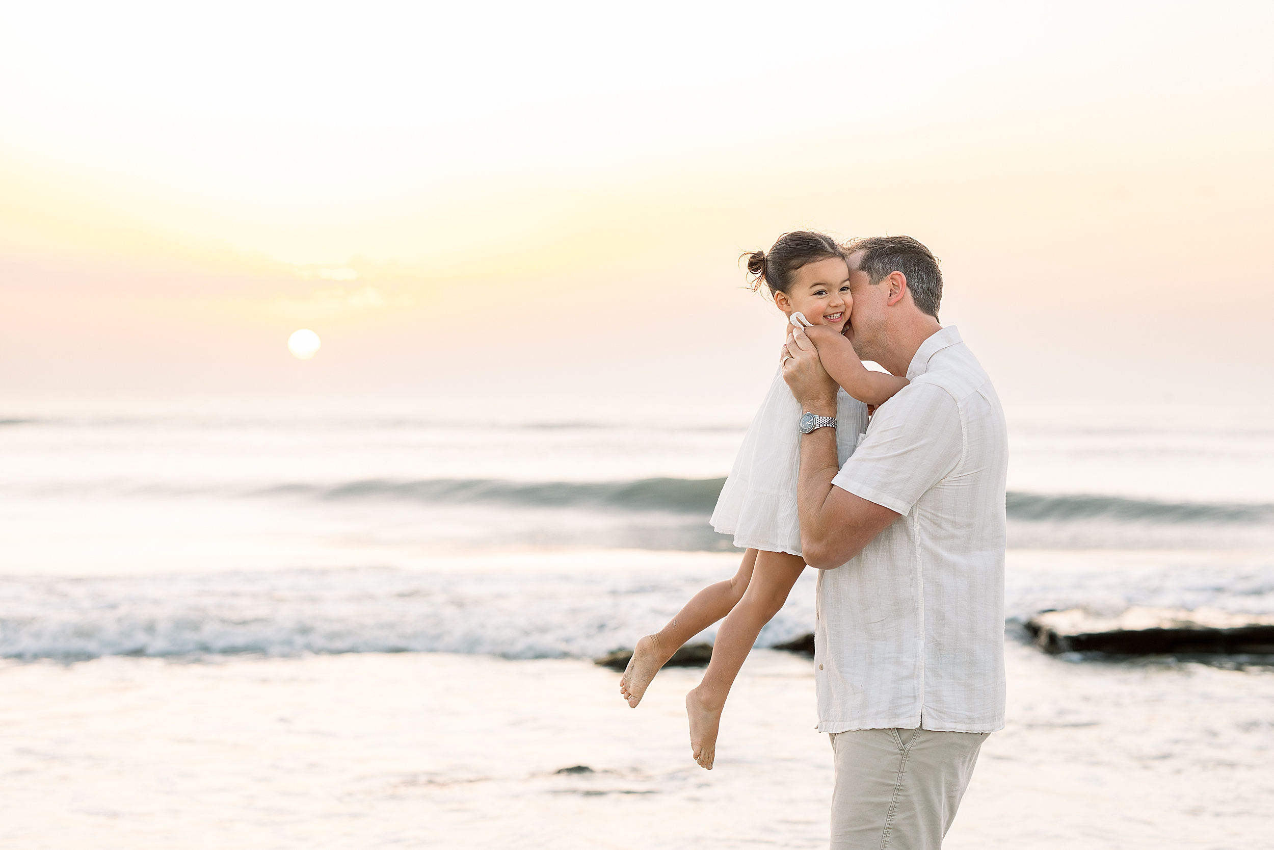 A man holds his little girl up in the air at sunrise on the beach in St. Augustine.