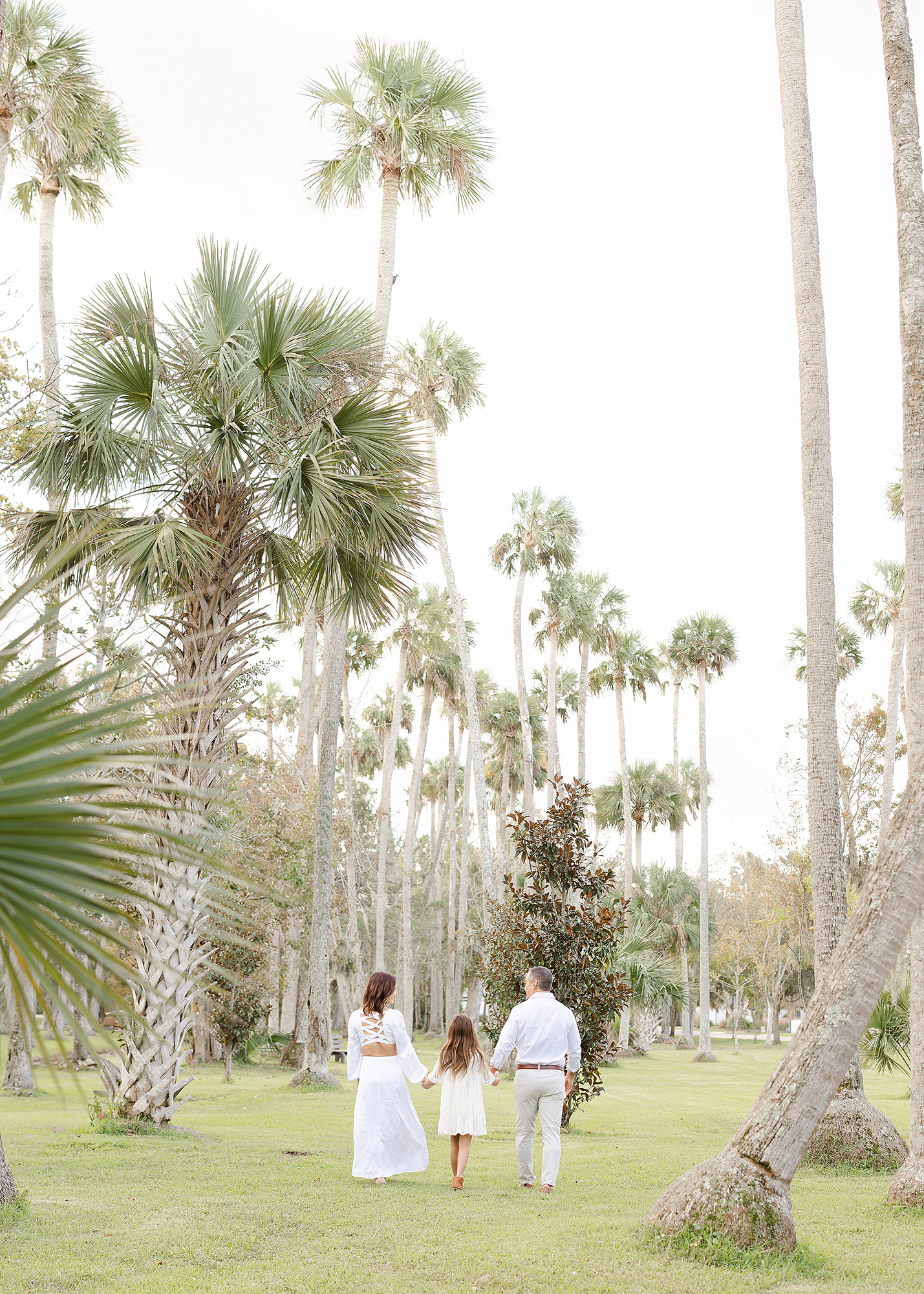 A landscape image of a family of three dressed in white standing in Johansen Park.