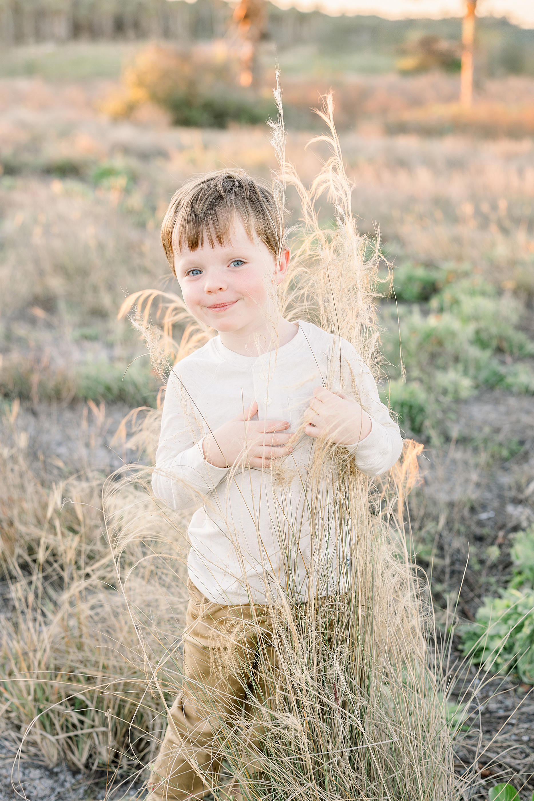 A little boy dressed in neutral clothing plays behind the bushes near the sand dunes in St. Augustine.