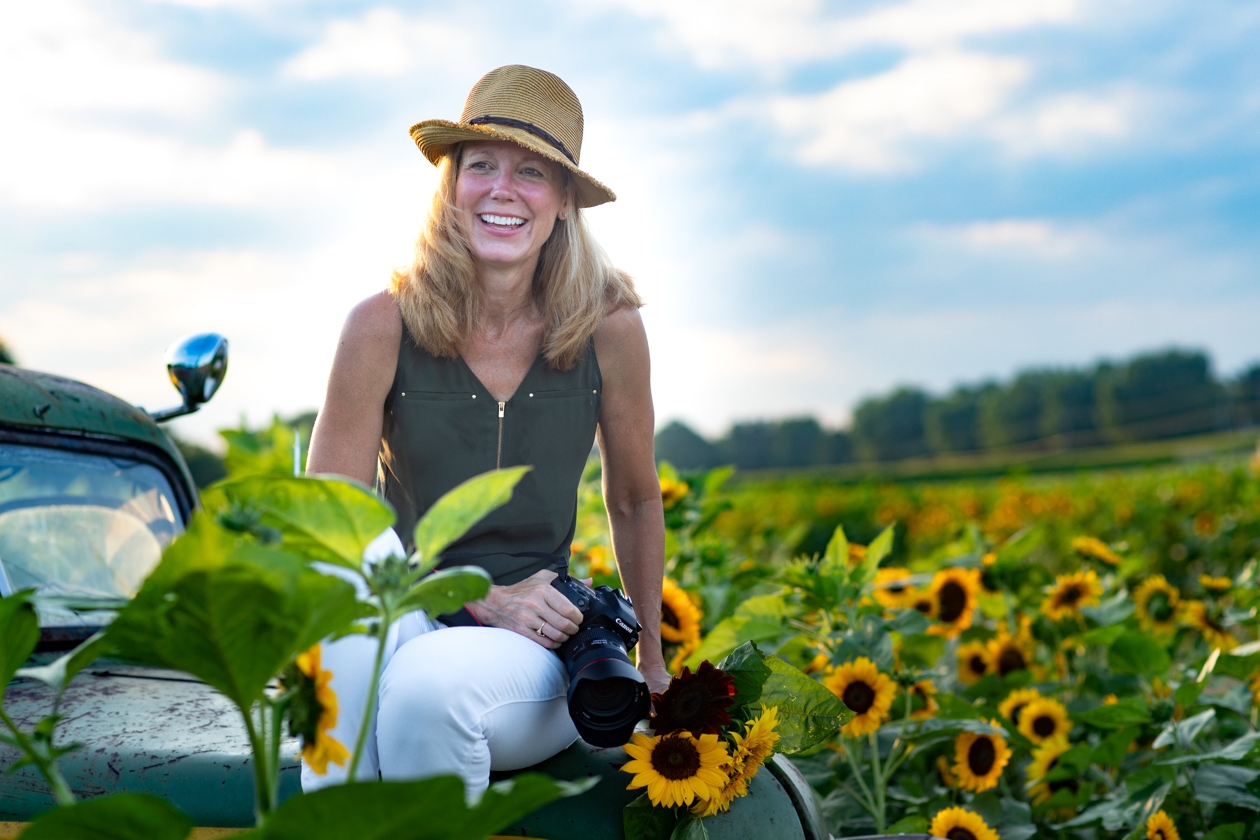 Female Photographer Sitting in Sunflower Field on Top of Old Truck