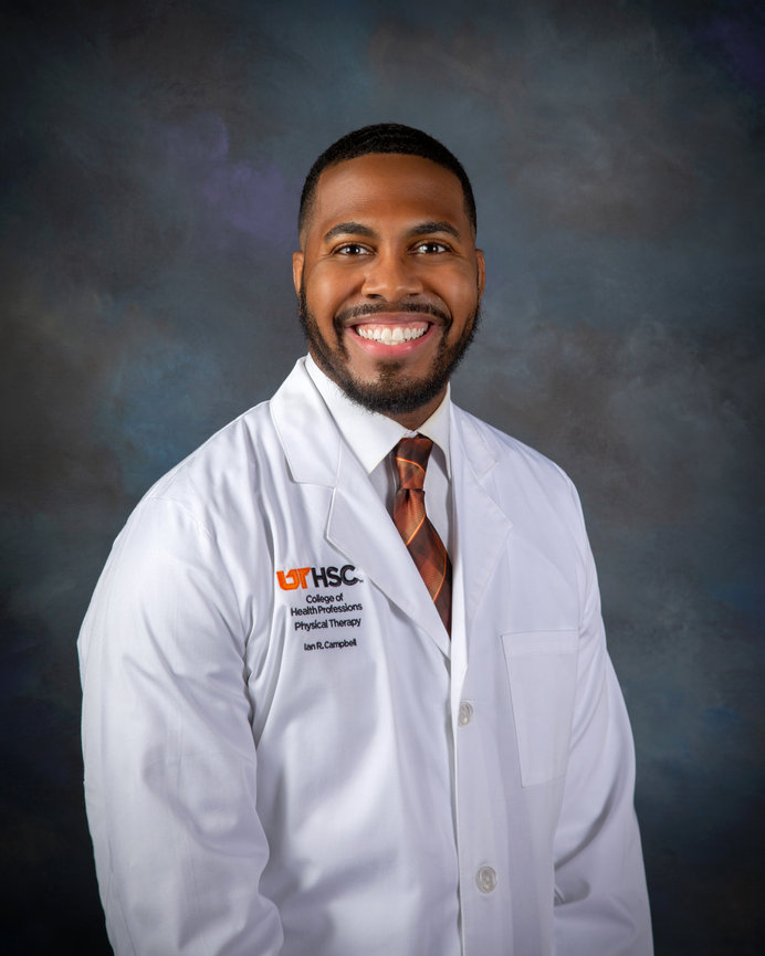 Man in white coat with a tie smiling against a dark, textured background.