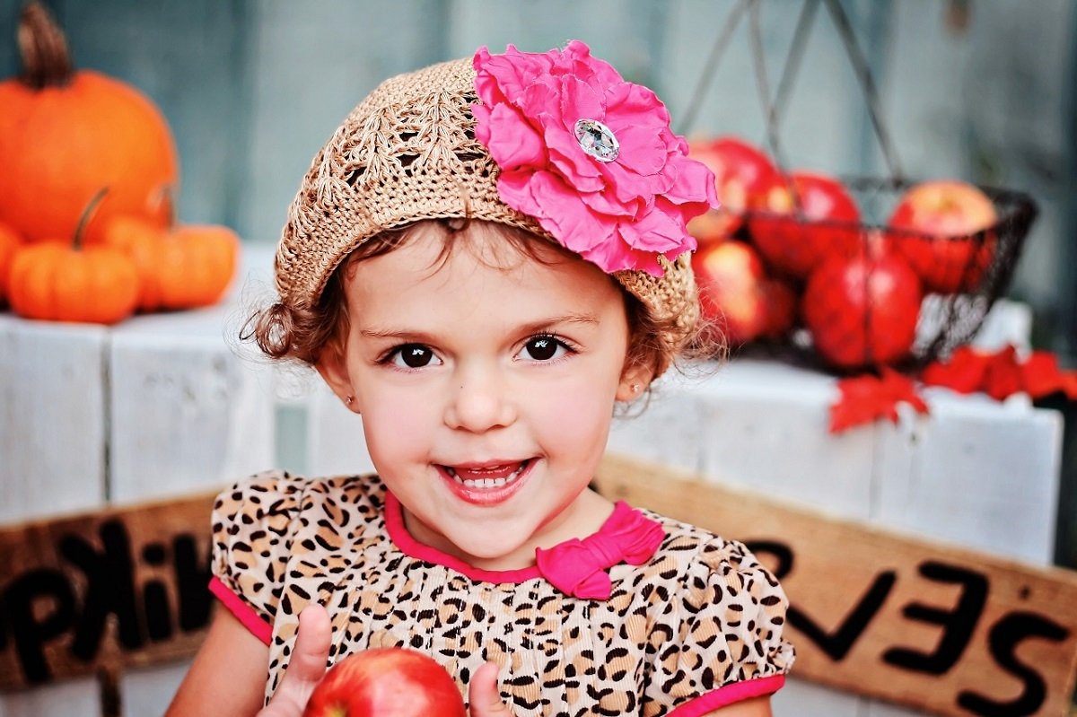 Little girl in bright colors holding apple in fall setting