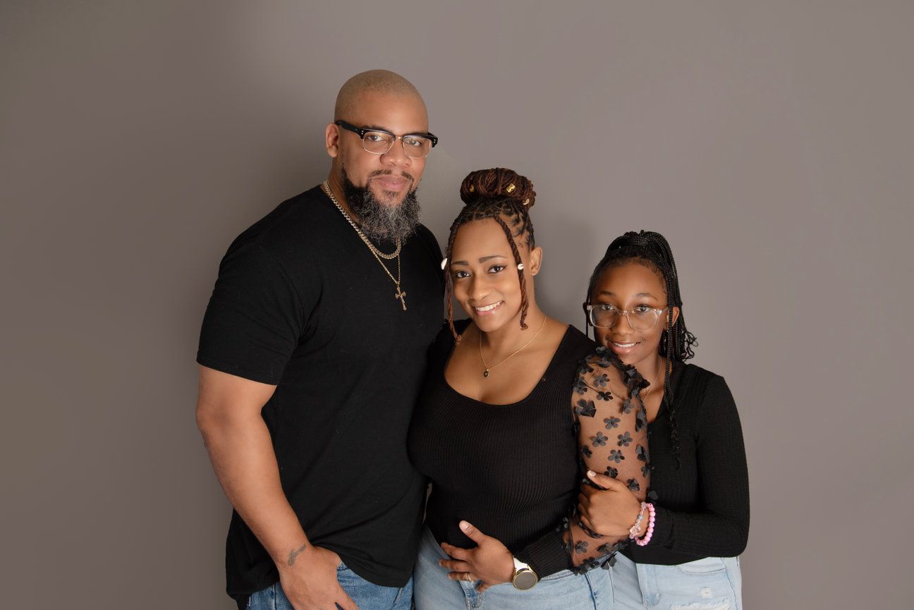 A family portrait featuring a father, mother, and daughter, all smiling against a neutral background.