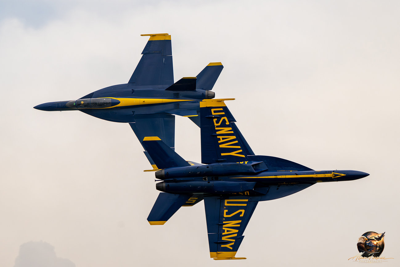 Two U.S. Navy Blue Angels F/A-18 Super Hornets passing in opposite directions during a precision aerobatic maneuver.