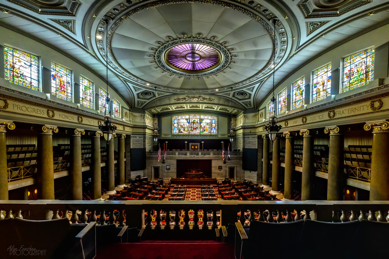 Ornate historic house chamber with stained glass windows, grand dome ceiling, and central judge's bench