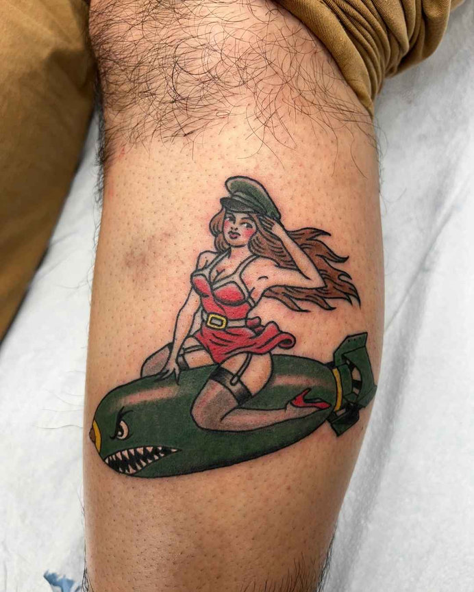 Retro pin-up girl tattoo riding a green bomb with military cap, red dress, and flowing hair made by Beam at Torch Tattoo in Anaheim, California.