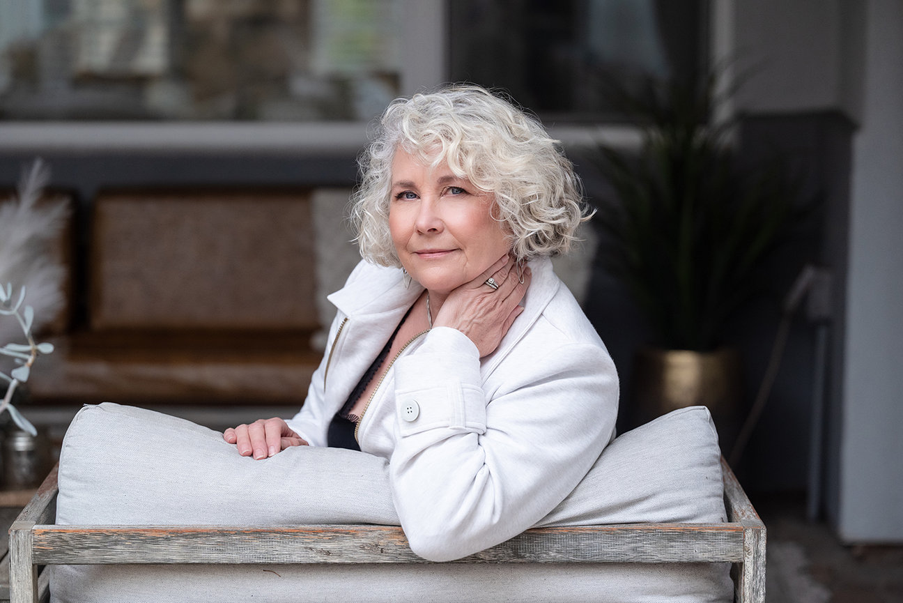 Blonde woman in white jacket sitting on sofa, by real estate photographer, Stefanie Blue.