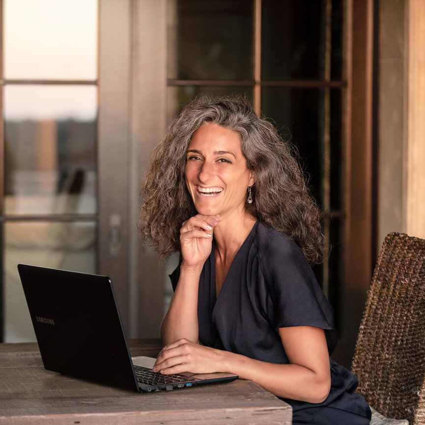 Happy female entrepreneur at an outdoor table with her computer, looking into camera with a big smile, by Southern California Personal Brand Photographer, Stefanie Blue.