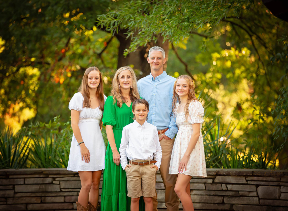 Classic close-up family portrait of five smiling together, captured in a refined style with soft outdoor lighting.