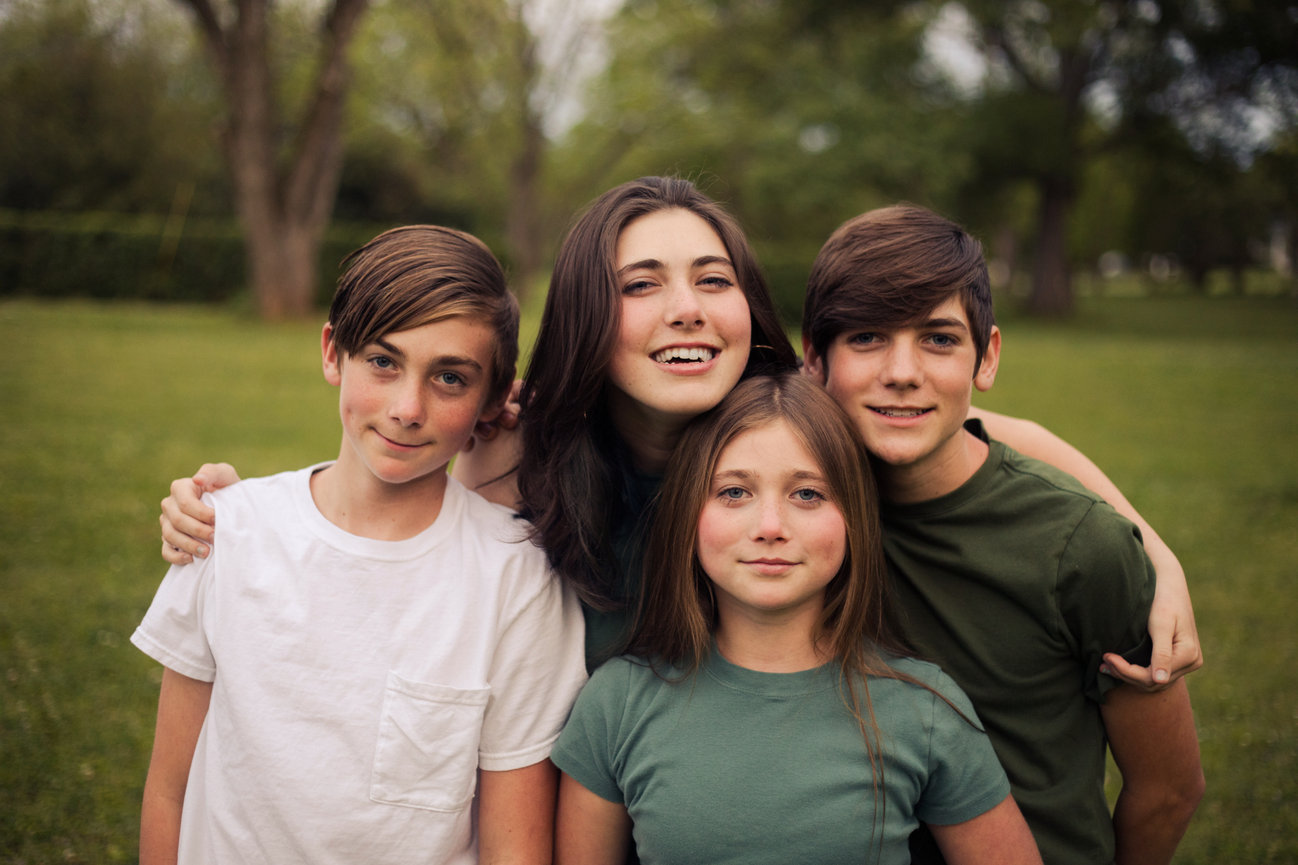 Four siblings posing together in a park with trees behind them.