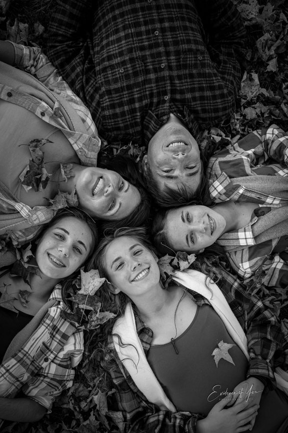 Group of six people lying on leaves in a circle, smiling, in black and white.