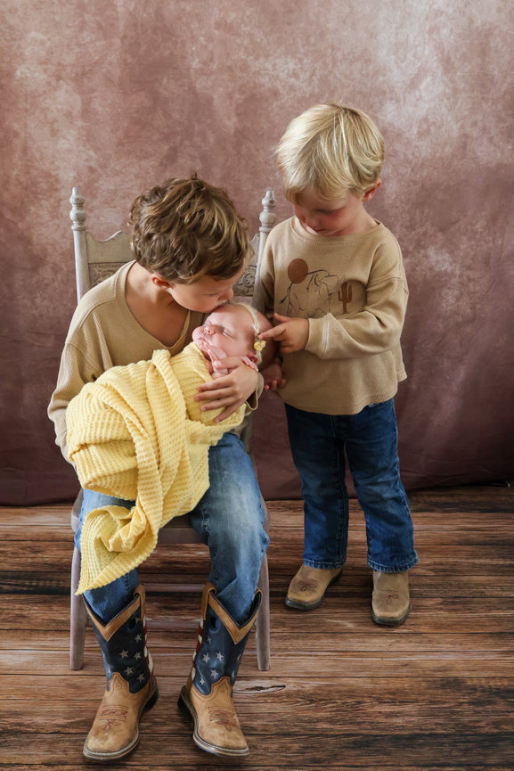 Two children standing together with a newborn baby in a family portrait