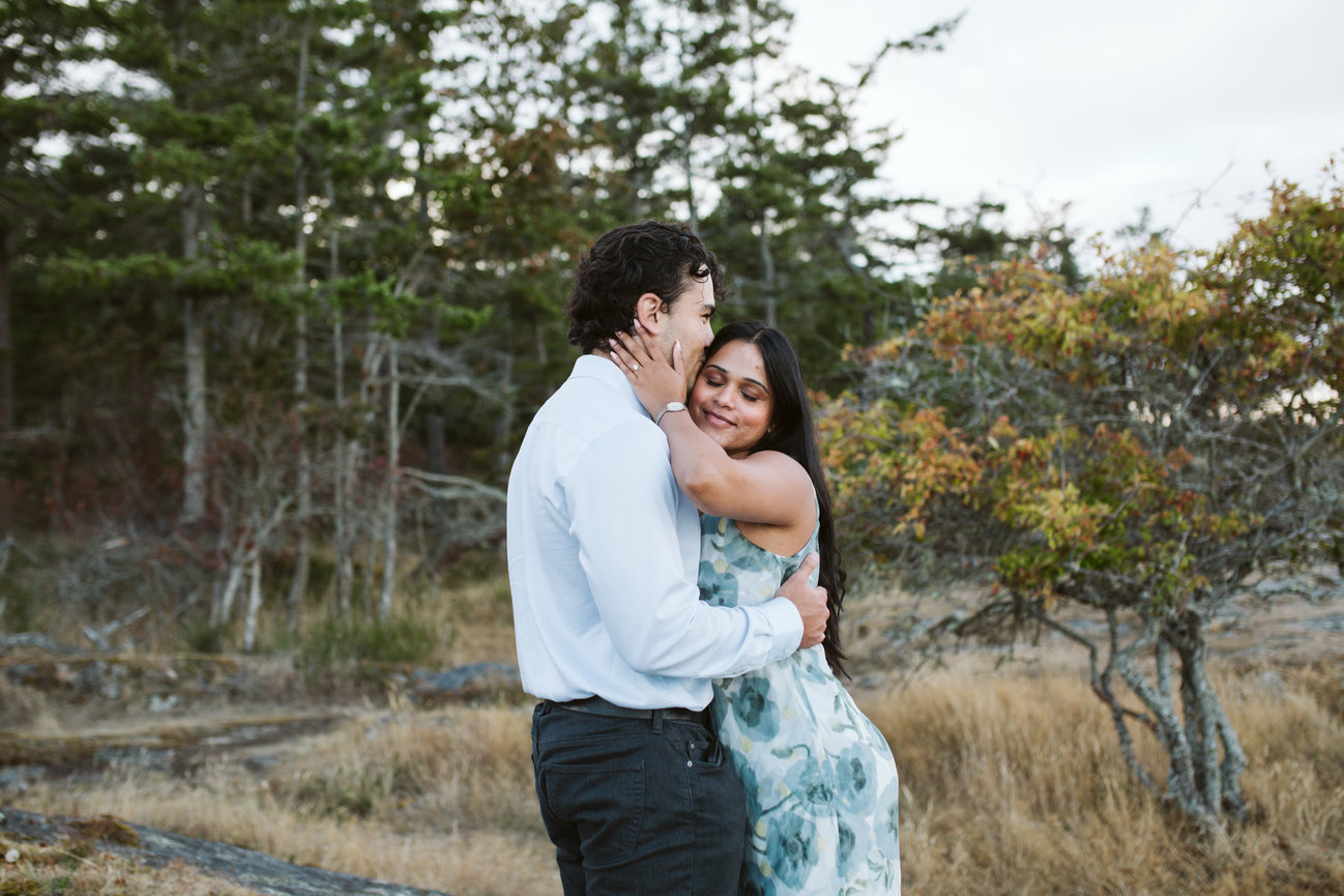 Newly engaged couple embracing beside coastal trees