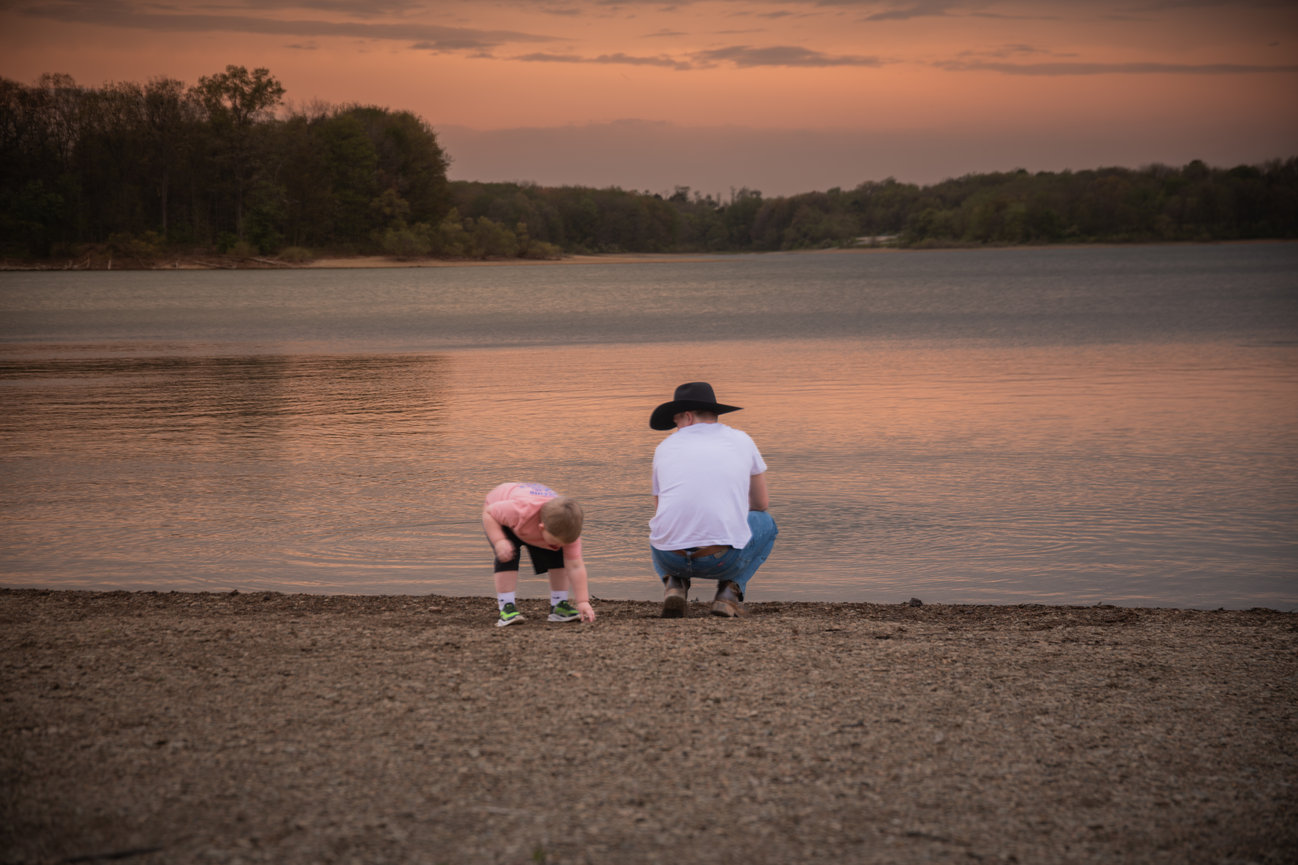 Father and child squatting by the lake at sunset