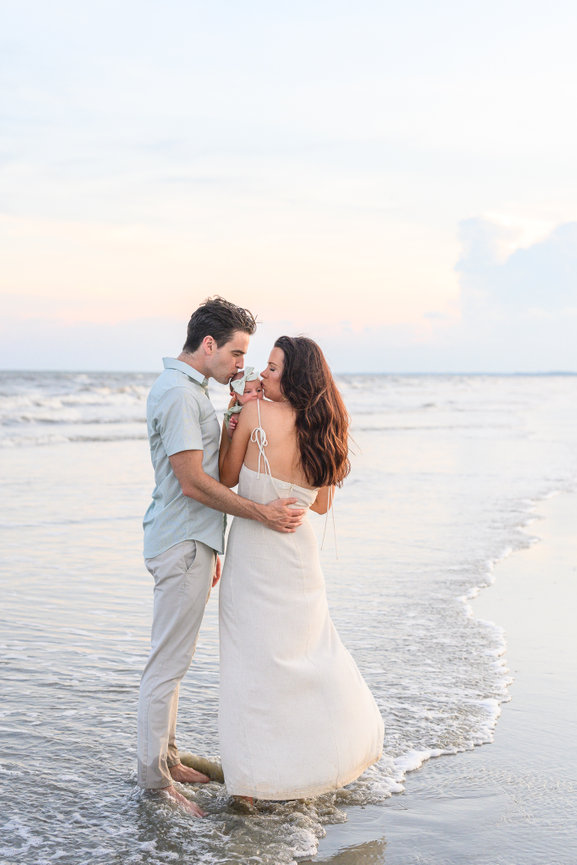 Couple embracing on the beach at sunset, with gentle waves touching their feet.