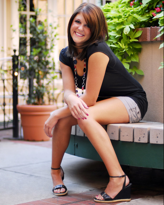 Smiling woman sitting on a bench in an outdoor setting with plants in the background.