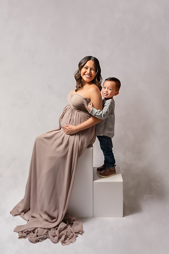 Dressy maternity image with son hugging his mom in a neutral Monmouth County photography studio.