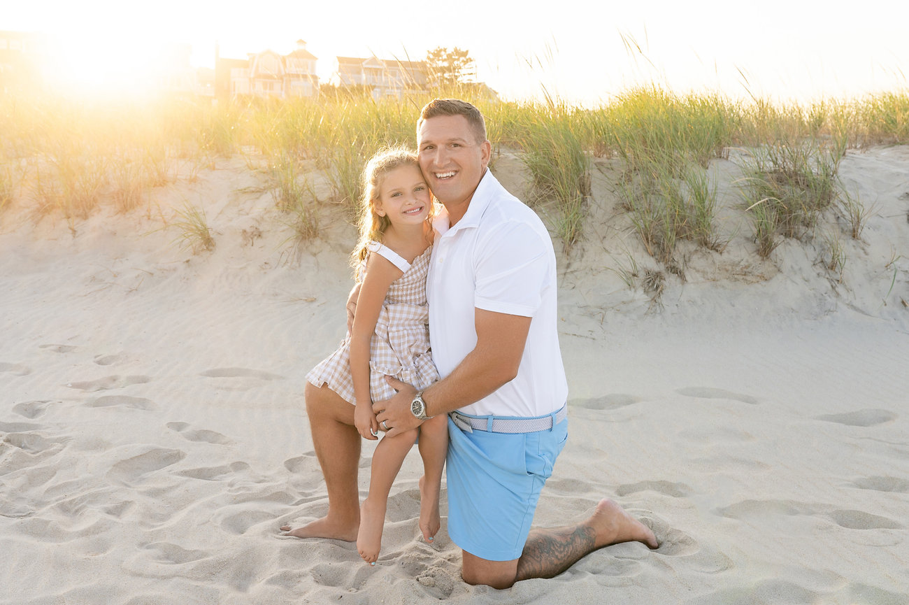 Dad twirling daughter in the sand with sunset in the background