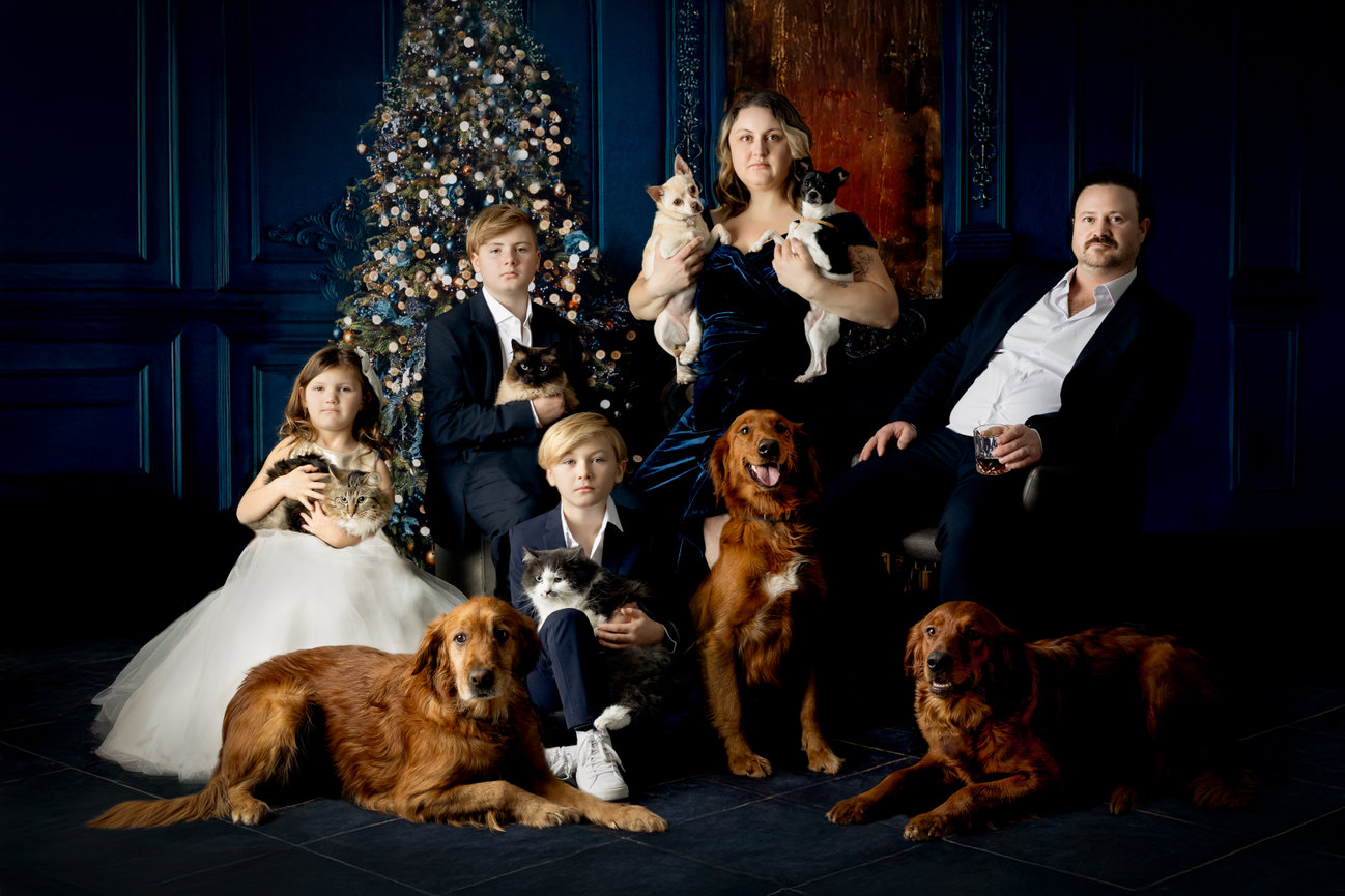 Family portrait featuring adults and children with several pets, posed in front of a decorated Christmas tree.