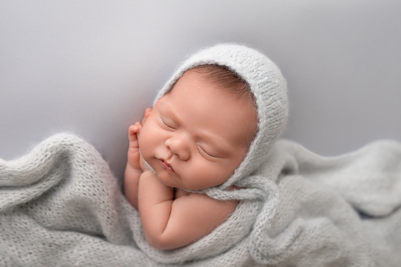 Modern newborn session on solid dusty blue background with soft lighting and clean composition