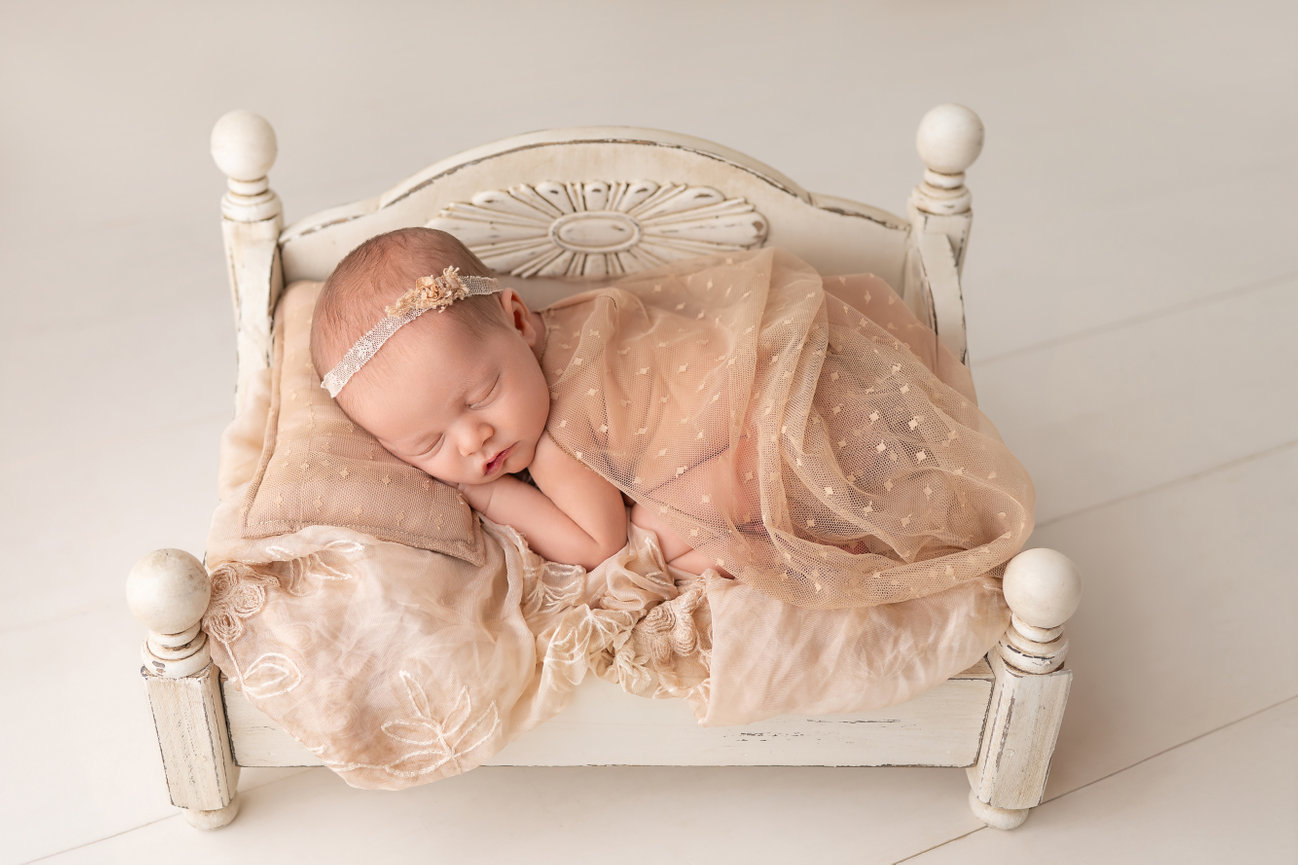 Neutral-toned newborn session with baby swaddled in oatmeal-colored wrap and styled in vintage daybed prop