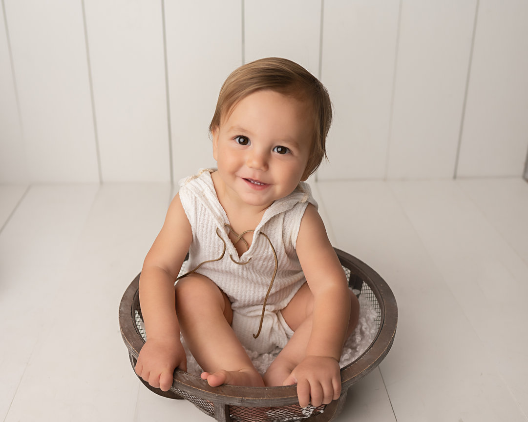 Baby in neutral outfit surrounded by soft, natural textures and white walls in Monmouth County studio
