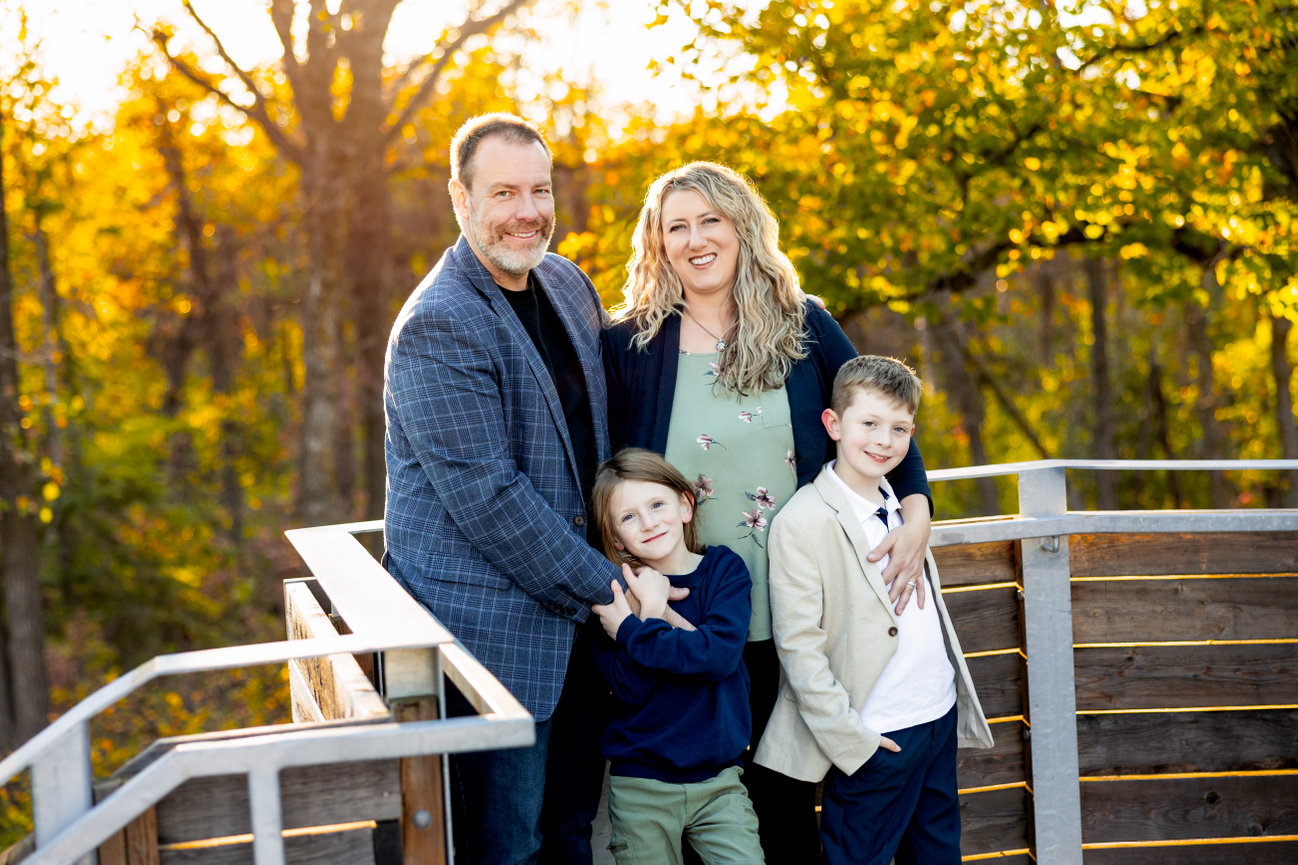 Family posing on a wooden deck in a forest with autumn foliage.