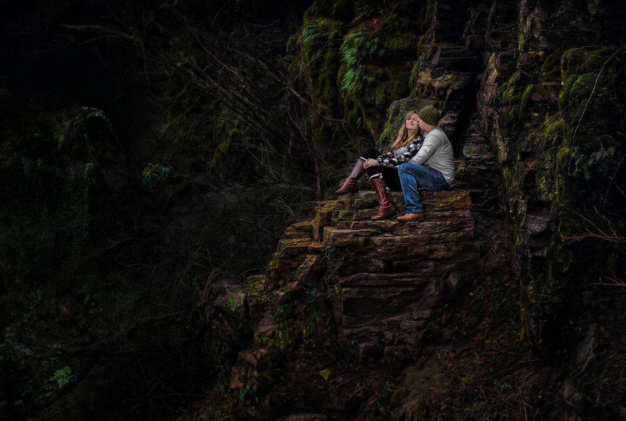 Person sitting on mossy stone steps in a dark forest.
