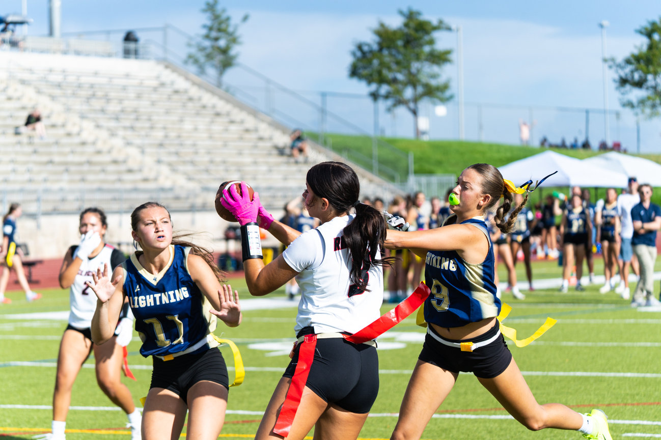 Flag football players reaching for the ball during a play on the field.