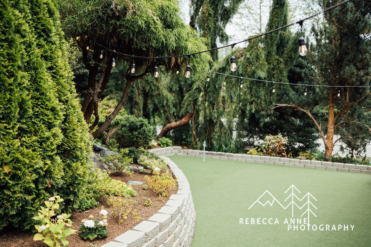 Beautiful garden with manicured lawn, lush trees, flowers, and hanging string lights.