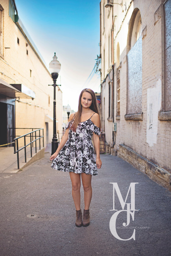 Young woman standing in a narrow sunlit street wearing a floral dress