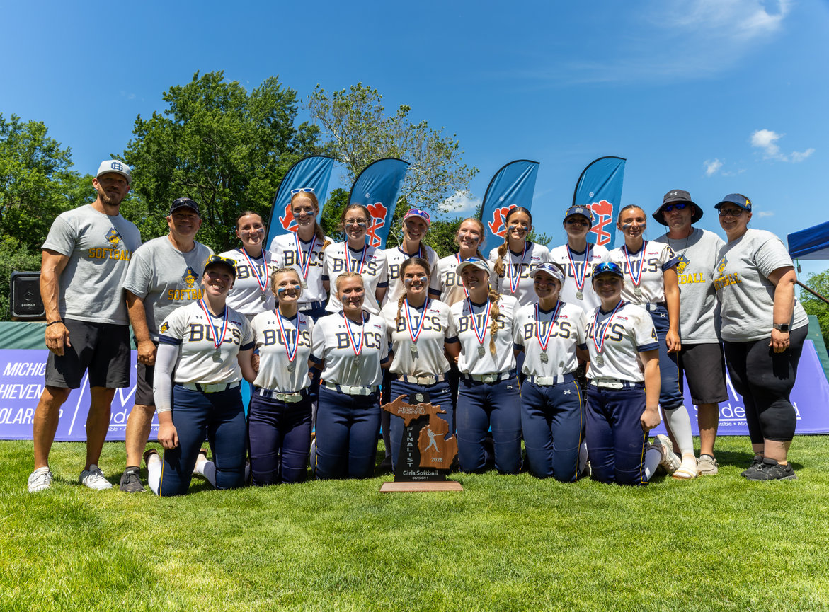 Softball team posing together on the grass outdoors.