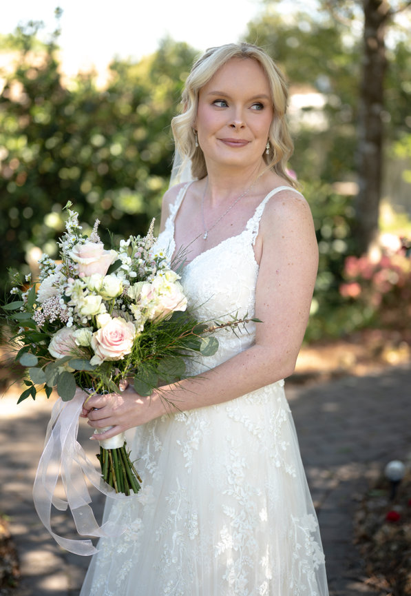 Bride in a white lace dress holding a bouquet outdoors.