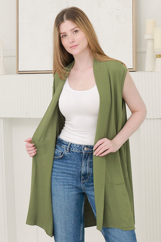 Model wearing green sleeveless cardigan over tank top and denim jeans in spring summer fashion photoshoot.