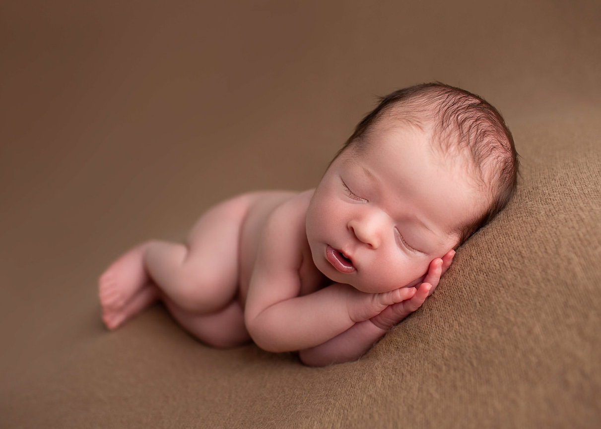 Newborn baby boy sleeping on his side in angel pose on tan background during his newborn photoshoot with newborn photography Dreamworks Photography in Kansas City photography studio