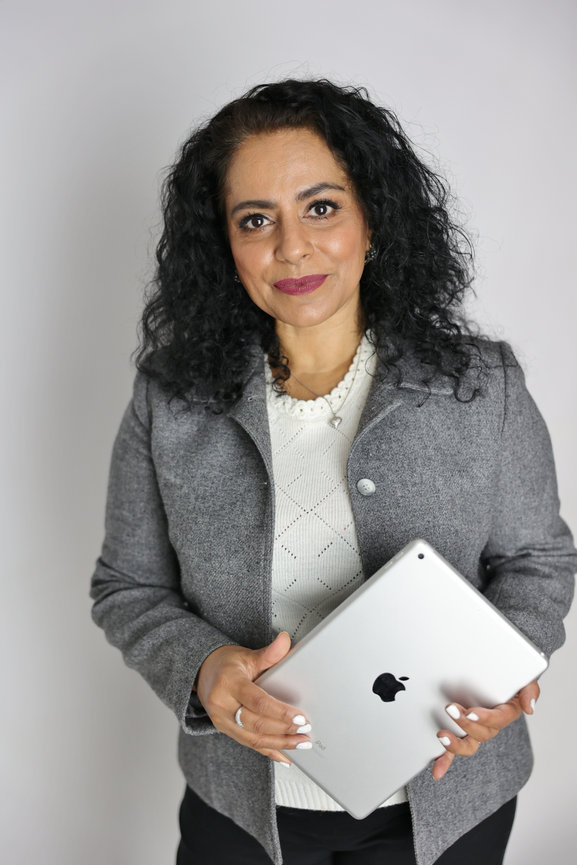 Woman holding a silver iPad, wearing a gray blazer and white top against a plain background. authentic photos for my business and website