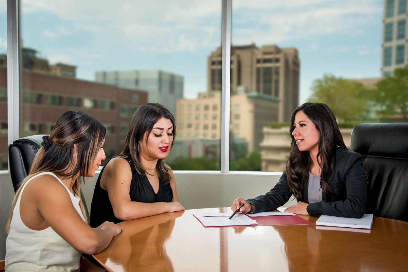 A female attorney in a boardroom consulting with two female clients.