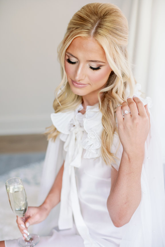 Beautiful blonde bride getting ready for her wedding day with champagne glass in her hand and engagement ring showing. Wedding photography by Heather Durham.
