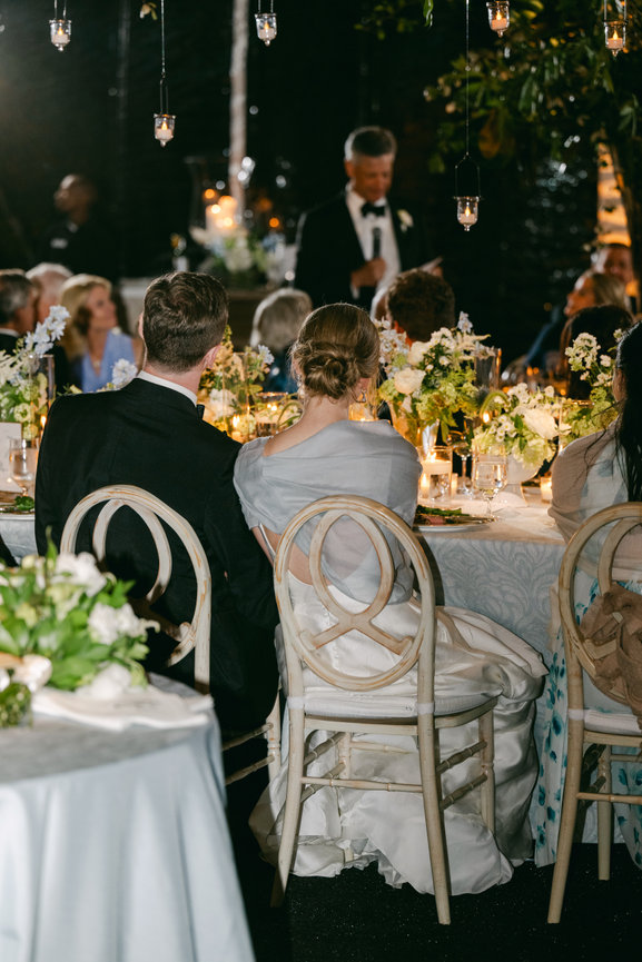 Bride and groom seated at wedding reception head table listening to speeches. Luxury wedding photography by Heather Durham.
