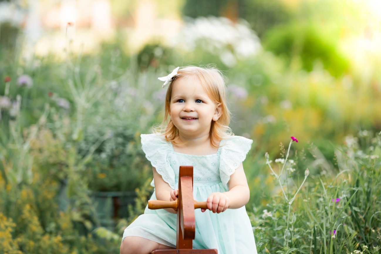 Little girl, child on wooden horse smiling outdoors in photography session