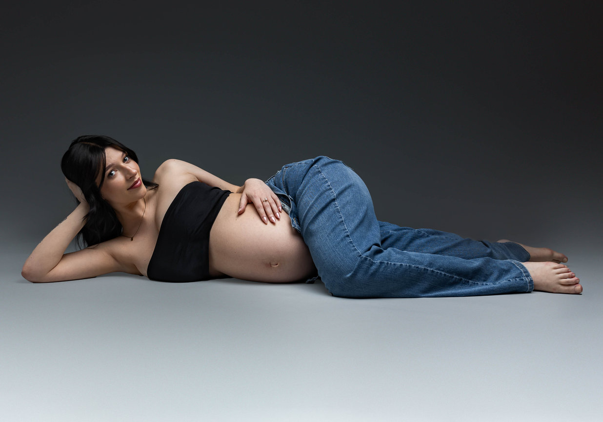 Expecting mother with hand on baby bump in jeans with neutral studio background