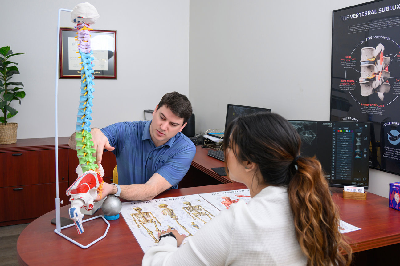 A professional explains a colorful spine model to a seated person in an office setting.