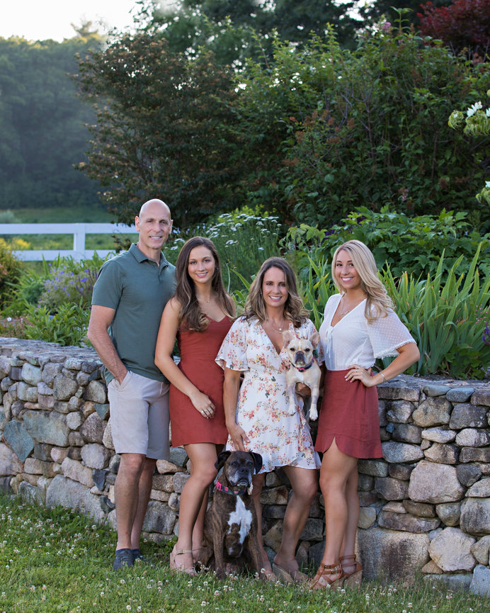 outdoor family portrait of parents and young adult daughters with boxer dog and French bulldog by stone wall and garden walpole ma