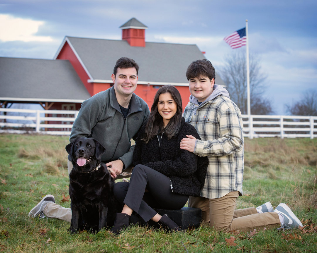 Outdoor family portrait of three teenaged siblings with black dog by red barn white fence American flag walpole ma