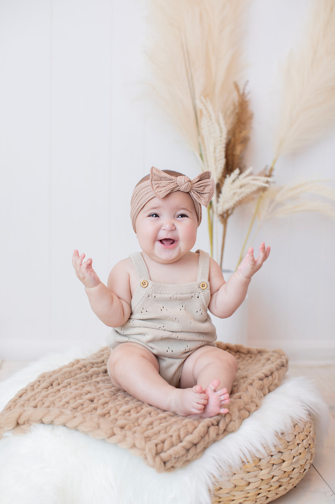 Baby raising one hand while sitting beside pampas grass
