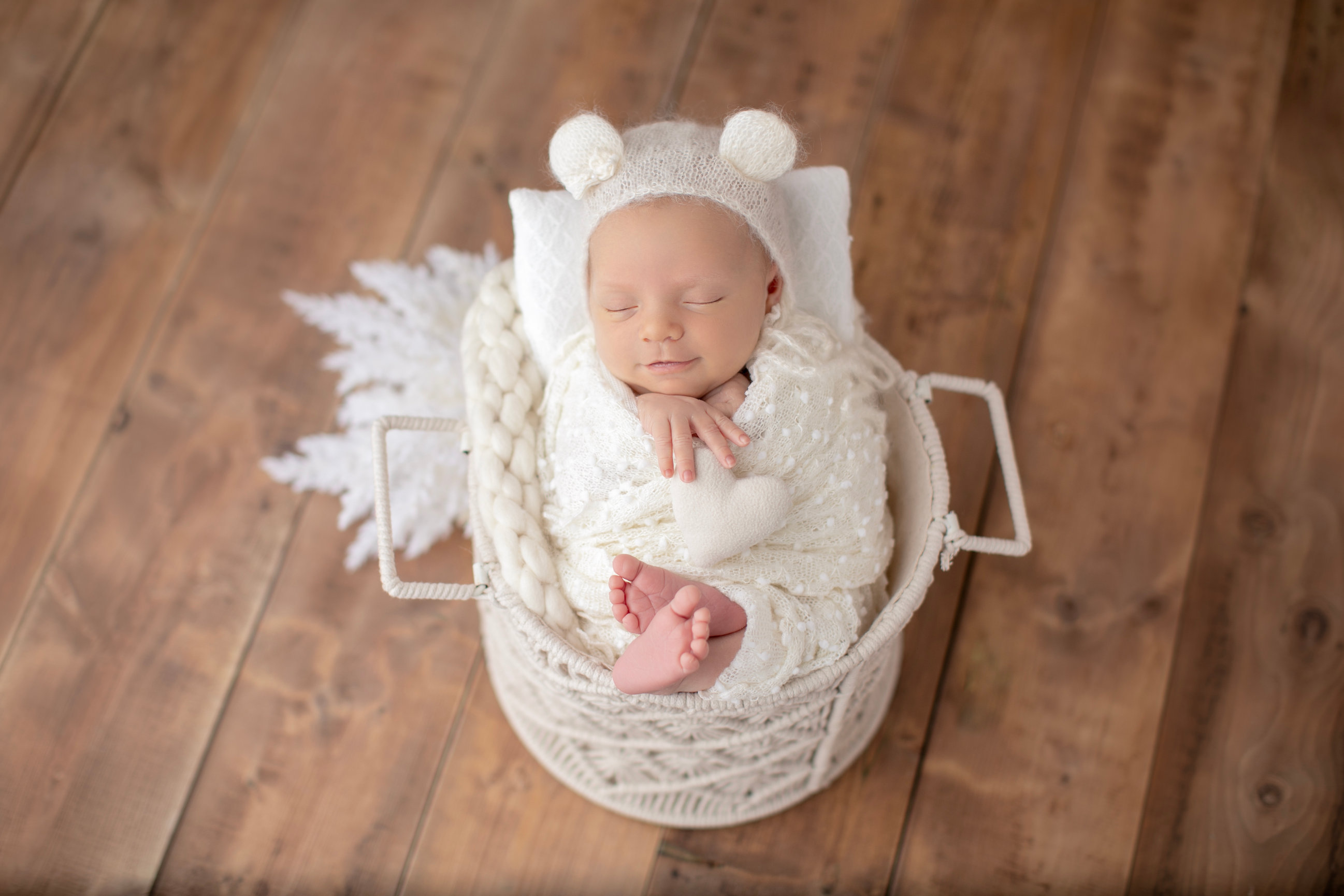 Sleeping newborn in a bear bonnet and cream wrap, nestled in a small white basket.