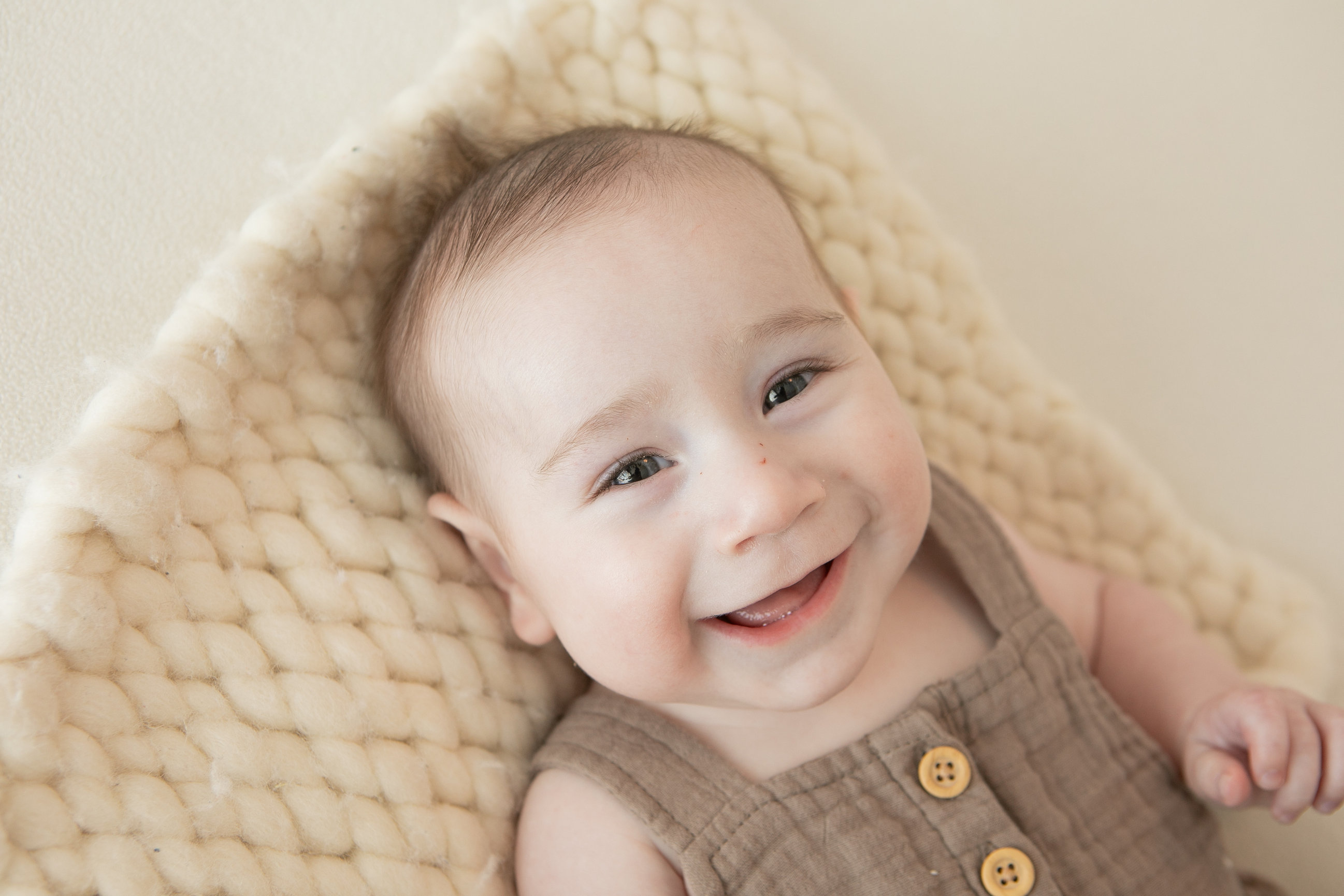 Baby in a brown romper smiling from a woven basket