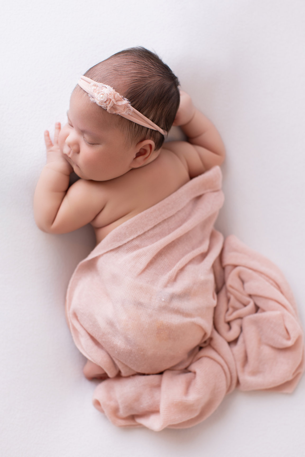 Newborn baby girl wrapped in a blush pink wrap on a white backdrop