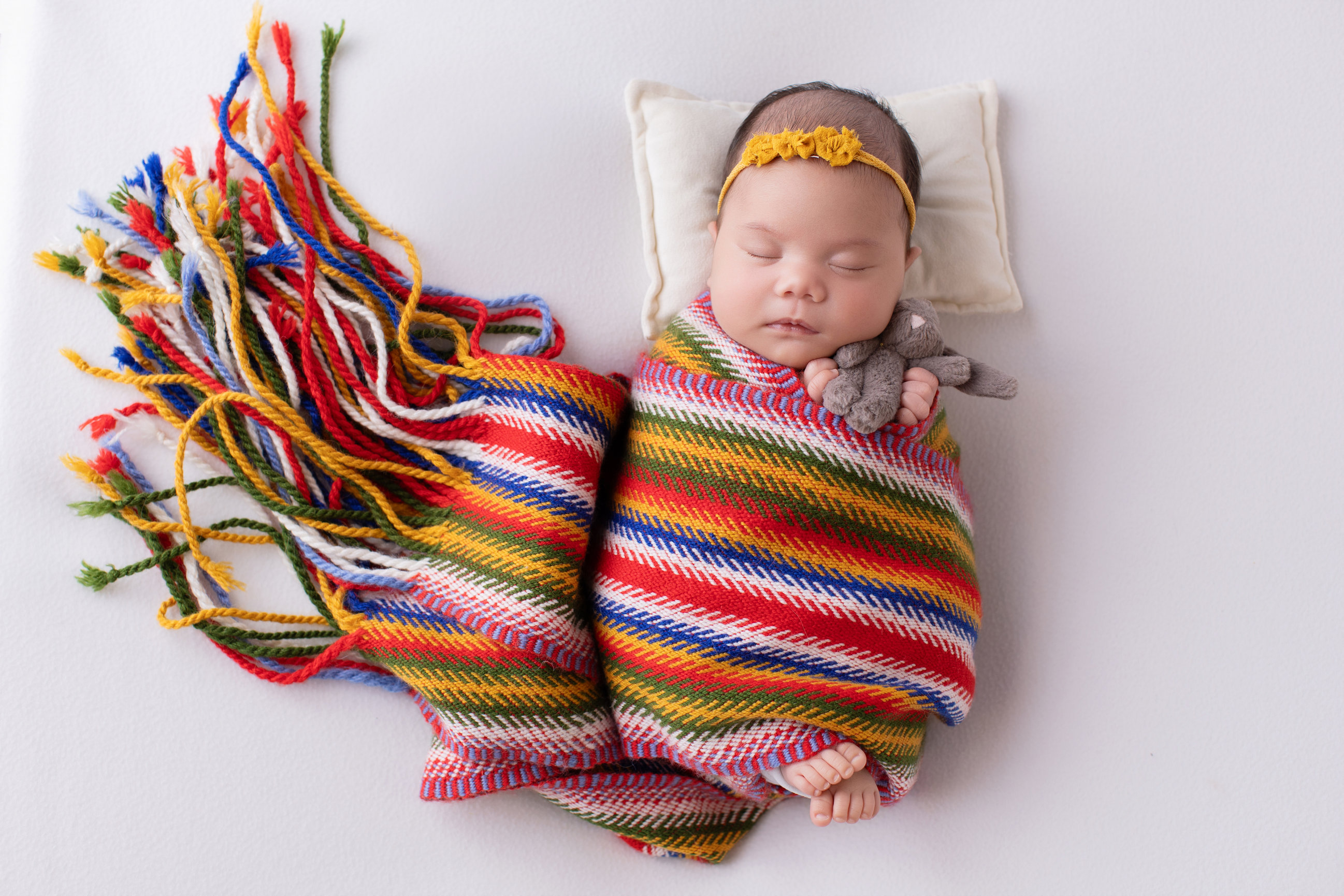 Newborn baby girl swaddled in a Métis sash on a white backdrop