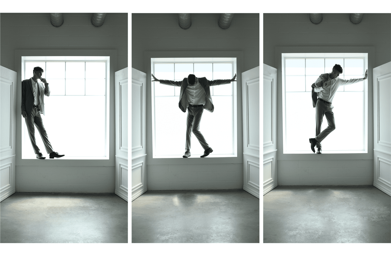 High school senior guy wearing a suit while standing in the window at Kliks Photography.